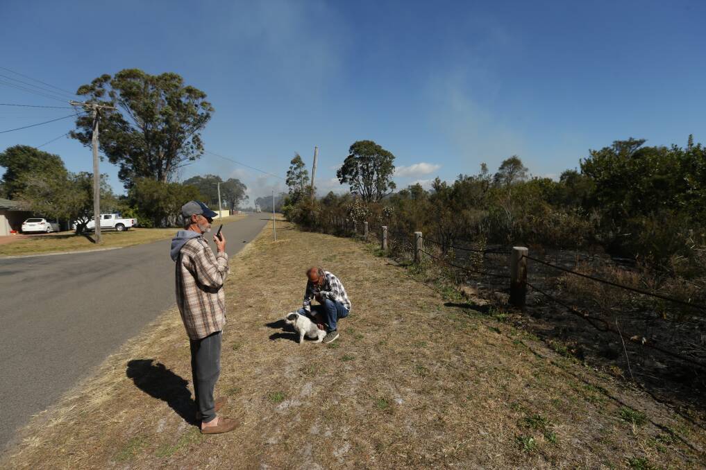Bushfires have burned overnight in Port Stephens. Pictures taken on Tanilba Ave, Tanilba Bay. Residents Mick Ryan, in the cap, and Darril Burgess, sunnies, and Laddie the dog. Picture: Jonathan Carroll  