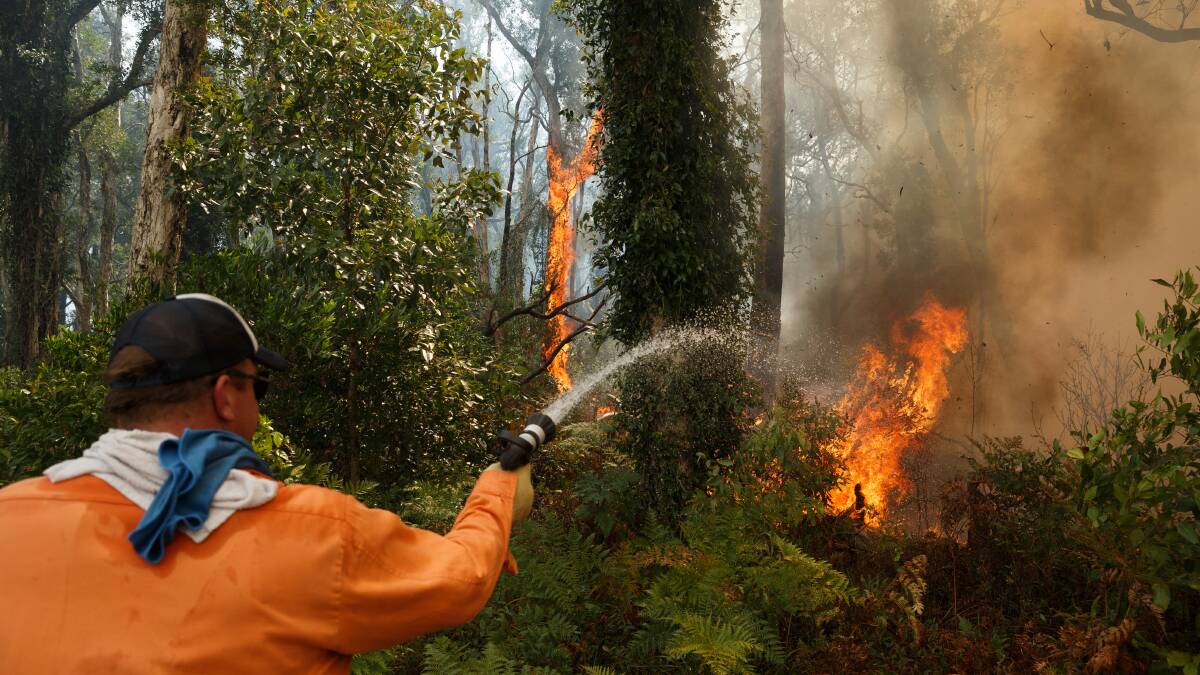 ALL HANDS: Nick Marshall fights the Tomago fire on Saturday at the house of friends Kane and Rhianna Gorfine, on Cabbage Tree Road. Picture: Max Mason-Hubers 