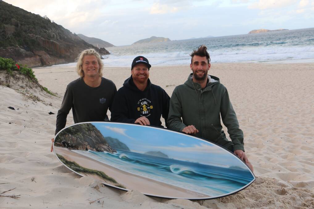 SHORE THING: Port surfers (from Left) Josh Stretton, Adam Dawkings and Kurtis Herman at Box Beach with the King of the Box surfboard to be raffled off at presentation night.