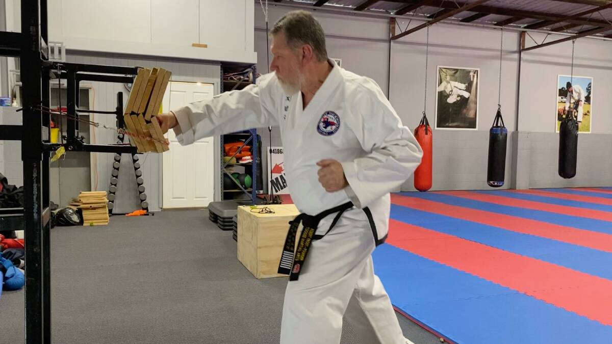 SMASHING: Grand Master Robert Frost breaks five boards with a punch at Raymond Terrace taekwondo headquarters. Picture: Supplied