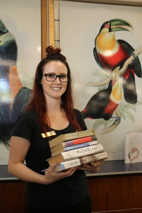 Port Stephens Library assistant Jessica Roberts standing in front of some of the bird illustrations currently on display at the Salamander Bay library, holding some of the most read books from 2017. Picture: Ellie-Marie Watts