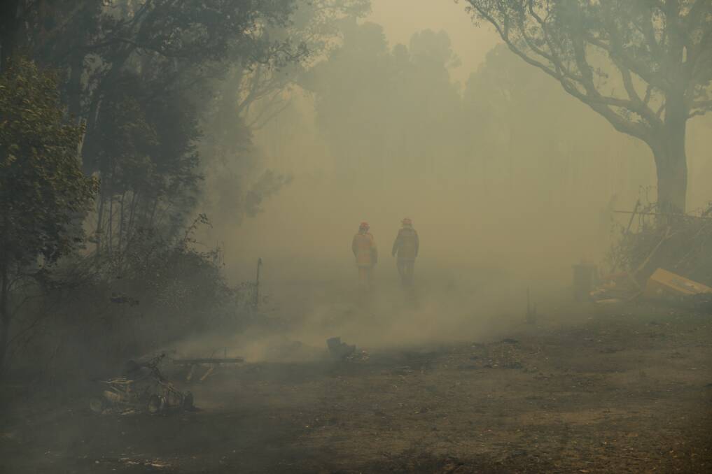 Firefighters walk through smoke after extinguishing the bush fire at Des Maslen's Williamtown property on Saturday. Picture: Jonathan Carroll 
