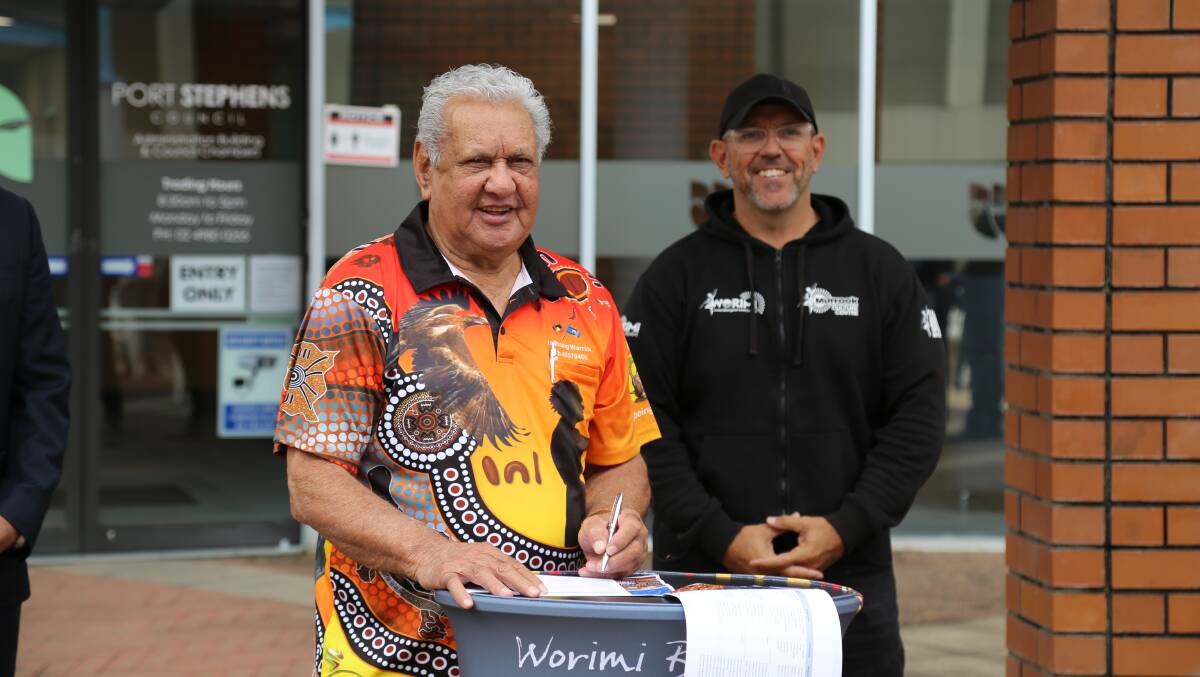 WELCOME BACK: Worimi elder Uncle John Ridgeway signing the Yabang Gumba-Gu agreement during the 2020 NAIDOC Week opening event, flanked by Worimi Local Aboriginal Land Council CEO Andrew Smith. 