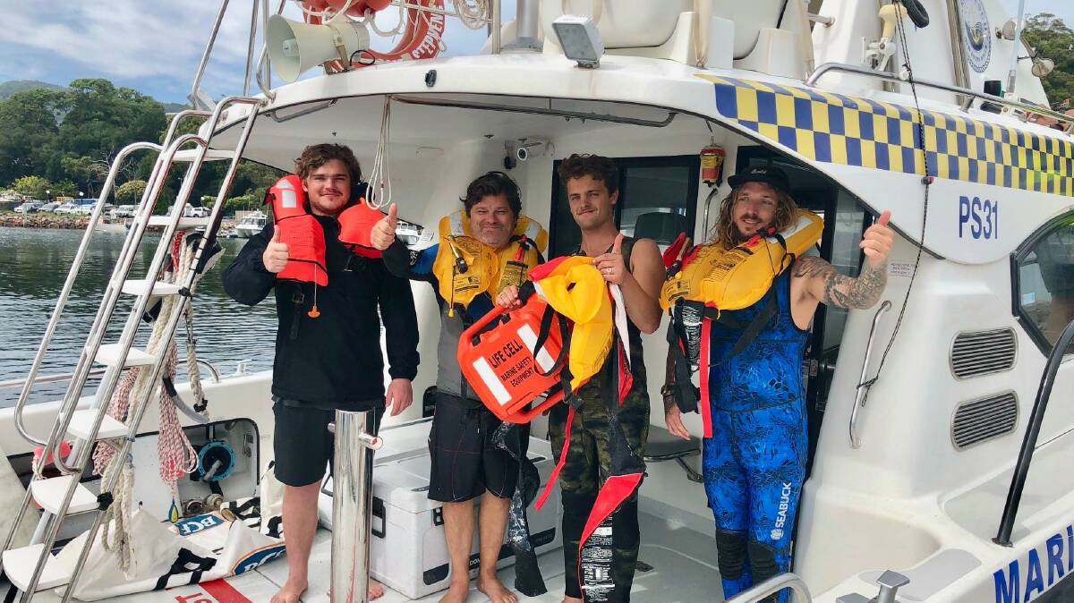 HIGH SPIRITS: Novocastrians Leo Hamilton, 21, Ian Hamilton, 57, Noah Hamilton, 23, and family friend Moritz, 26, on a Marine Rescue vessel back at Nelson Bay on Monday. Noah can be seen holding the Life Cell they used. Picture: Facebook/Marine Rescue Port Stephens